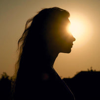 The silhoutte of a woman with long hair is slighly obscured by the sunlight coming from behind her where her eye is, creating a lense flare