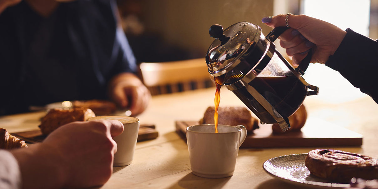 Artisan Coffee being poured from a cafetiere into a mug with people sitting around a table