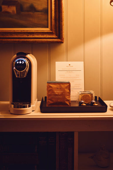 In a hotel room, Artisan Coffee bags and paired chocolates sitting in a display case next to a pod machine