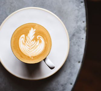Latte art poured into the top of a latte in a white cup and saucer on a metal table