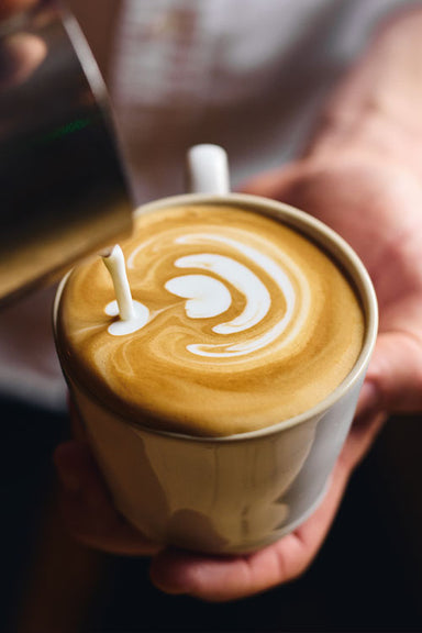 Latte art being poured into a latte in a white mug by a professional barista