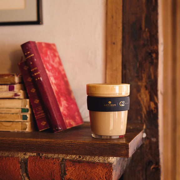 An Artisan Coffee Co branded travel mug on a fireplace mantle next to some old books