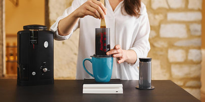 woman makes coffee with aeropress sraight into a blue cup surrounded by brewing equpiment