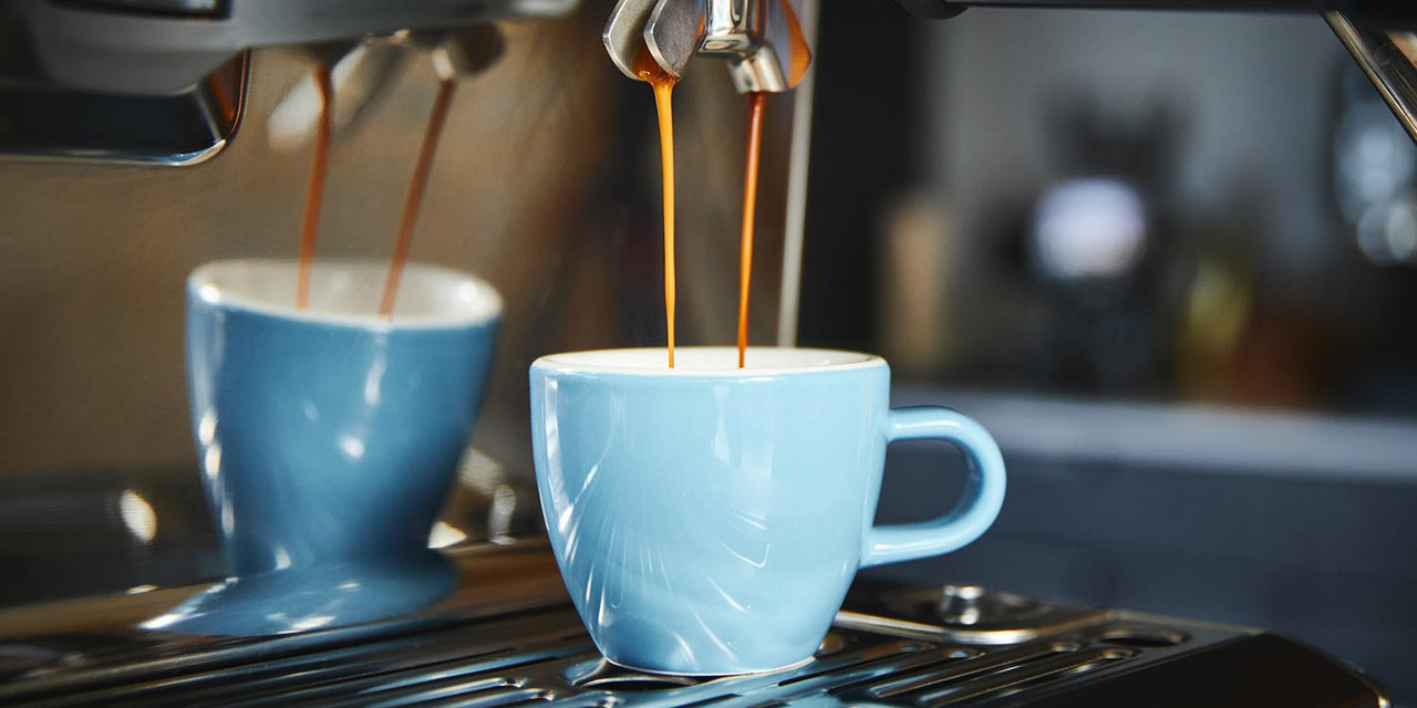 Artisan-coffee-is-running-out-of-a-porter-filter-on-an-espresso-machine-into-blue-ceramic-espresso-cup-the-reflection-of-which-can-also-be-seen-in-the-machine
