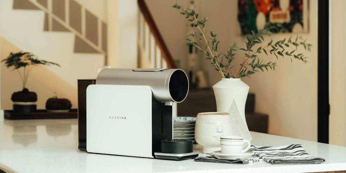 The Morning Pod Machine in white on a counter top with coffee making accessories in a stylish kitchen