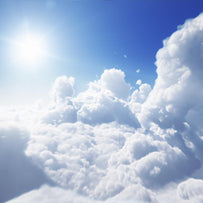 Fluffy white clouds are infront of a perfect blue sky with the sun shining at us