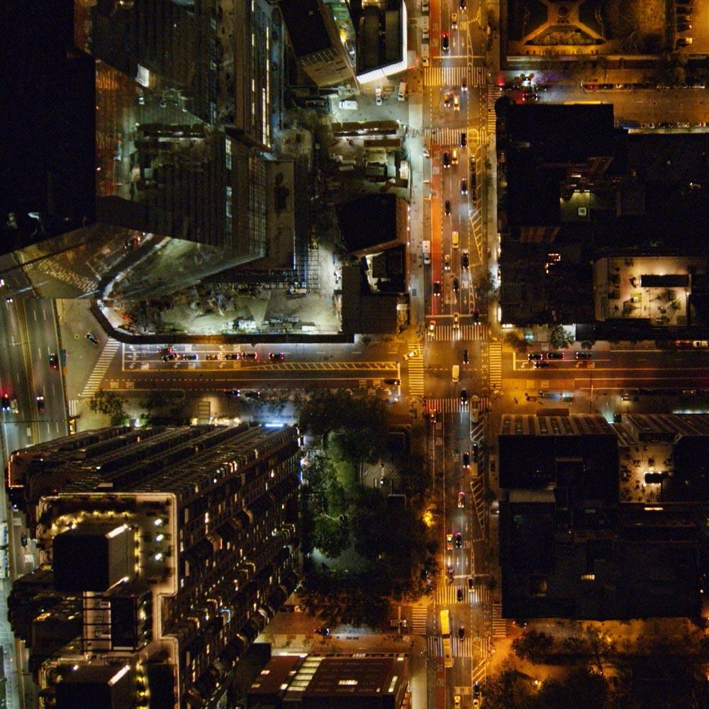 An aerial shot of a city scape at night time, street lights are on and cars are on the roads