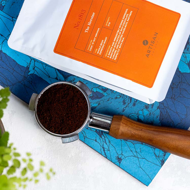 The Heroine Whole Bean Coffee with a porta-filter from an espresso machine that is full of ground coffee
